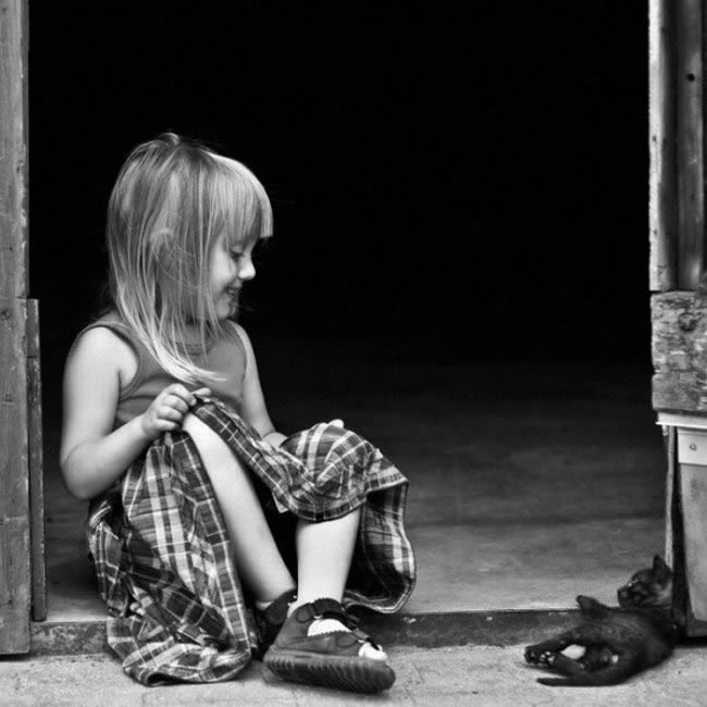 девочка в клетчатом платье сидит в дверях и напротив лежит чёрный котёнок, girl and kitty (black and white photo)